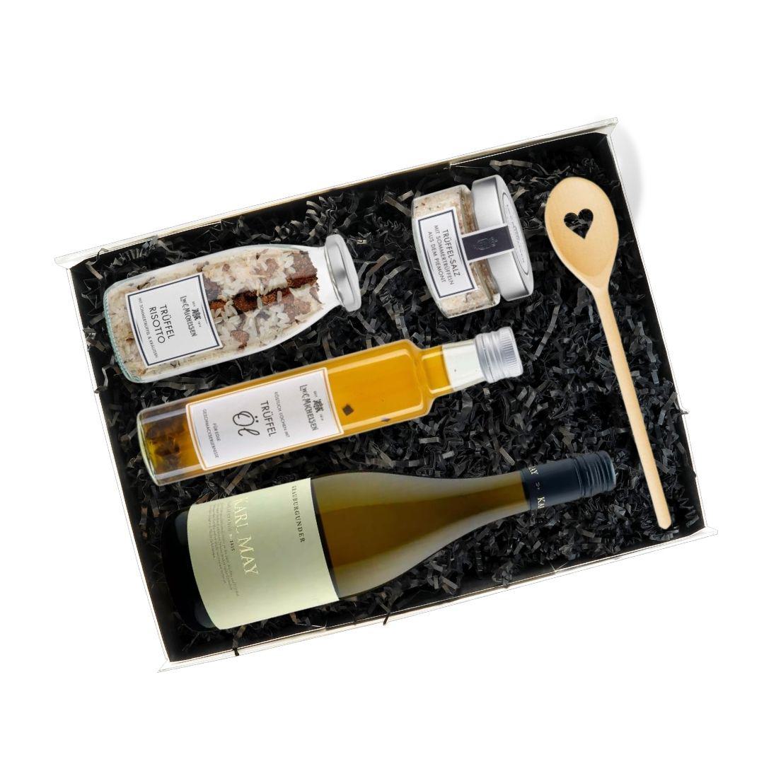 Geöffnetes Gourmet-Geschenkset mit Trüffelöl, Trüffelrisotto, Trüffelsalz, Holzlöffel und Weißwein auf schwarzem Füllmaterial arrangiert