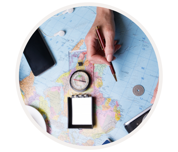 Hand, die einen Stift über einer Landkarte hält, mit Kompass und Notizblock zur Reiseplanung.