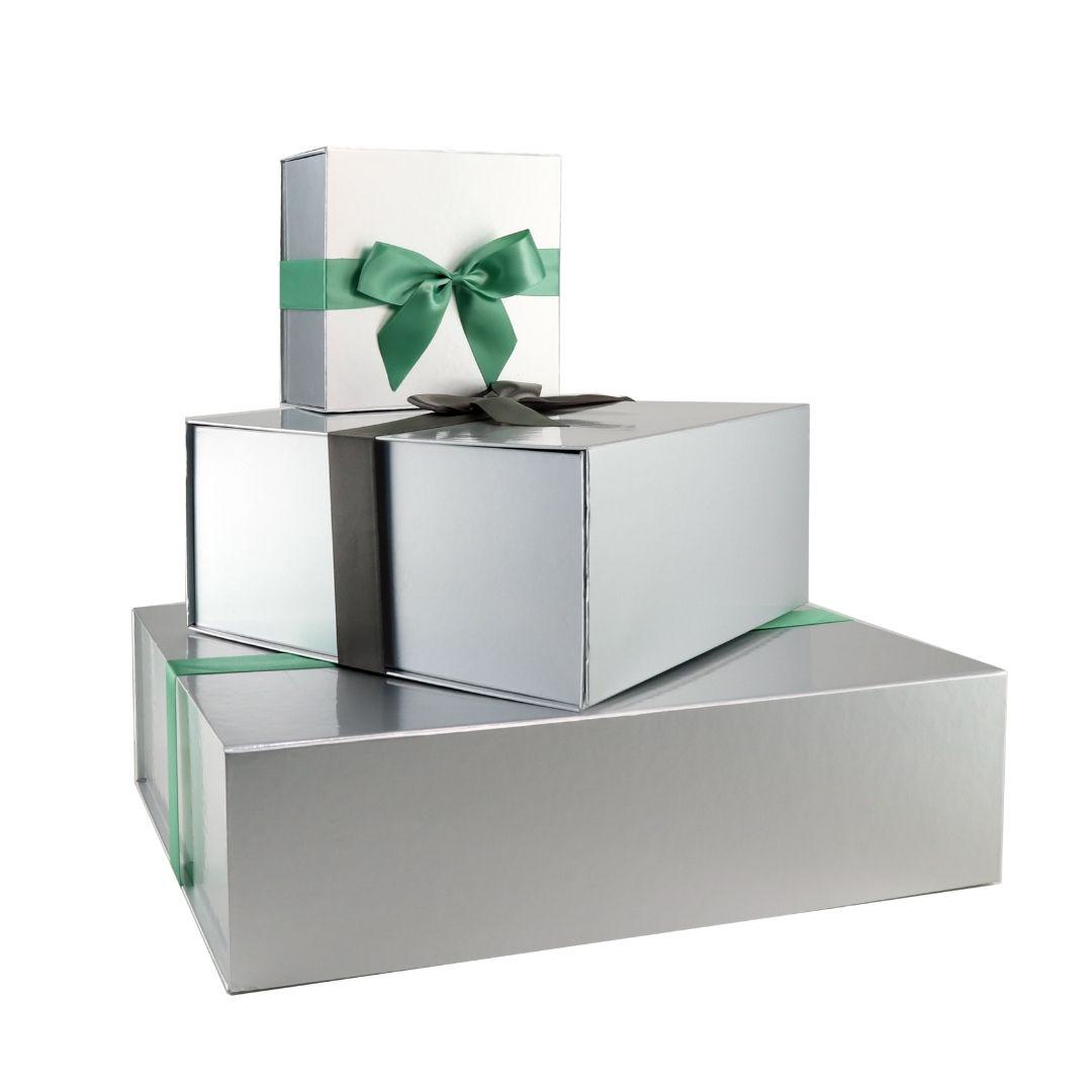 Mehrere elegante silberne Geschenkboxen in verschiedenen Größen mit dekorativen Schleifen in Grün und Grau gestapelt
