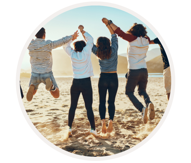 Zwei Männer und zwei Frauen springen fröhlich zusammen am Strand bei untergehender Sonne, halten sich an den Händen